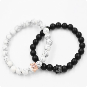 Dettaglio di bracciali in turchese bianco e pietra lavica con ciondoli a corona per coppia
