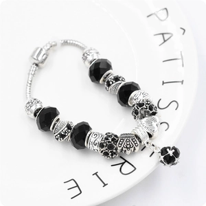 Dettaglio di un bracciale con perle sfaccettate nere e ciondoli a corona in argento