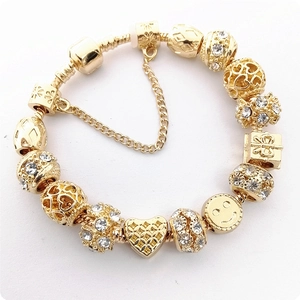Close-up of gold beaded bracelet featuring crystal heart charms and smiley face pendants
