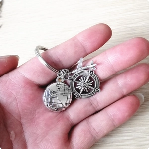 Vintage silver earth plane compass keychain with travel charms held by hand
