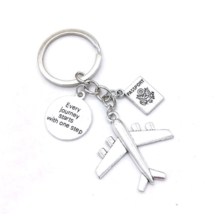 Silver metal travel keychain with airplane, passport charm and engraved quote on white background