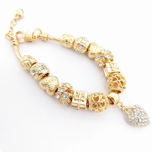 Détail d'un bracelet doré à perles avec cœurs évidés et breloques en zircon brillant