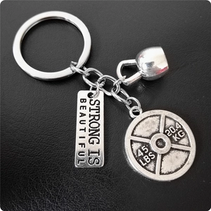 Détail d'un porte-clés fitness en métal avec disque d'haltère, kettlebell et pendentif motivant