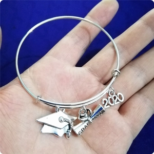 Detail van zilveren armband met afstudeerhoed en 2020-bedels op blauw fluweel