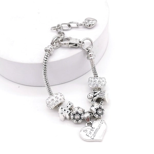 Detail eines silbernen Schlangenarmband mit First Communion Herzanhänger und Kreuz-Charm