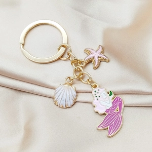 Detail of mermaid starfish and shell charms on golden keychain with satin background