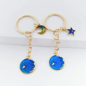 Detail of blue enamel star and moon gold keychains set on a minimalist white pedestal