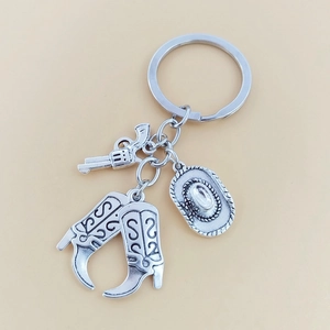 Détail d'un porte-clés western en argent vieilli avec revolver, bottes et chapeau de cowboy
