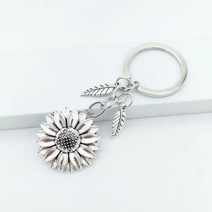 Vintage sunflower keychain with silver metal petals and feather charms on white stand