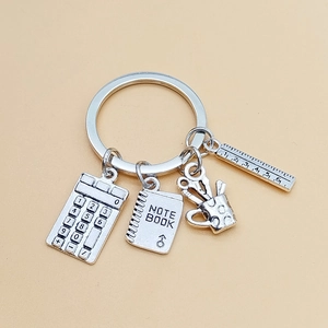 Macro shot of silver stationery charms featuring calculator, notebook, and ruler keyrings