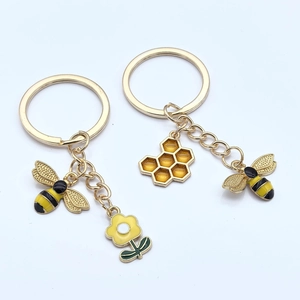 Vue détaillée des porte-clés émaillés abeille et alvéole avec breloques fleurs dorées