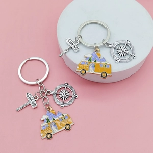 Détail de porte-clés de camping avec camping-car et boussole sur fond rose pastel