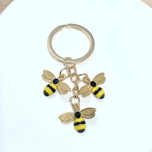 Détail de trois breloques abeilles en émail sur un anneau porte-clés en métal poli doré