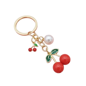 Golden cherry keychain with red fruit pendants, green leaves and a white pearl charm