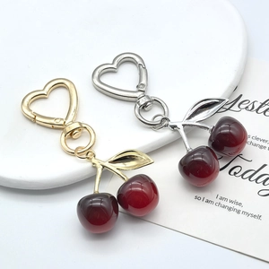 Detail view of red cherry keychains with heart-shaped metal clasps and leaf accents