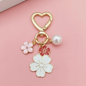 Detalle de llavero dorado de corazón con dijes de flores de cerezo y una perla blanca