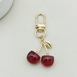 Close-up of cute acrylic red cherry keychain with gold metal lobster clasp and leaf detail