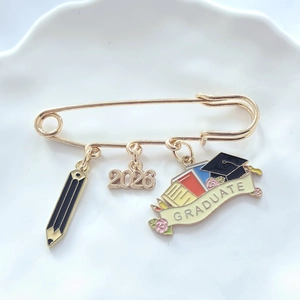 Detail of 2026 graduation brooch with pencil, cap, and graduate scroll charms