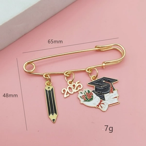Golden 2025 graduation brooch with black pencil and graduation cap charms on pink card