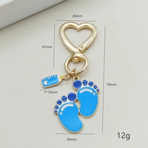 Detail van blauw geëmailleerde babyfles- en voetjesbedels aan gouden hartvormige sleutelhanger