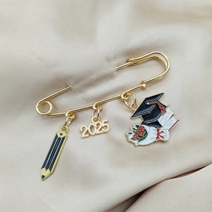 Macro detail of 2025 graduation brooch with pencil, year charm and mortarboard on satin