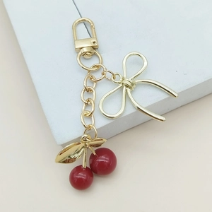 Porte-clés cerises 3D avec nœud doré élégant présenté sur un socle géométrique moderne