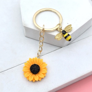 Vue détaillée du porte-clés tournesol doré et pendentif abeille sur pierre blanche