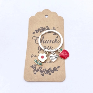 Détail du pendentif cœur Thank You, pomme rouge et fleur sur un porte-clés argenté