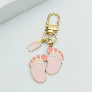 Close-up of pink enamel baby bottle and footprint charms on a gold metal keychain