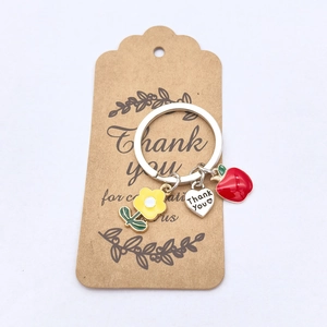 Détail des breloques en émail pomme et fleur sur un porte-clés cœur Thank You
