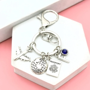 Close-up of travel keychain with silver airplane, globe, passport and blue gemstone