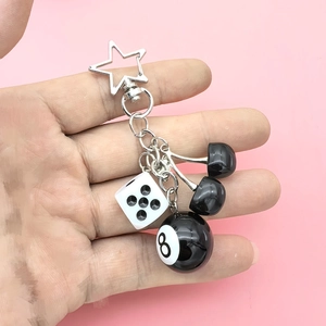 Detail of cherry, dice and billiards 8 ball keychain being held against pink background