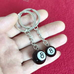 Close-up of two black number 8 pool ball keychains held in hand with silver metal chains