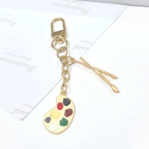 Dettaglio di un portachiavi dorato artistico con tavolozza di colori e pennelli