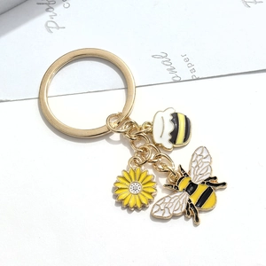Détail des breloques abeille, tournesol et pot de miel sur un anneau doré de porte-clés