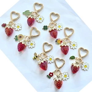 Détail de porte-clés fraise rouge translucide avec clips cœur dorés et breloques émail