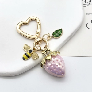 Gros plan du porte-clés fraise avec boucle coeur, abeille et feuille sur plateau blanc