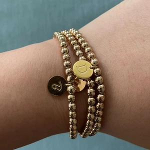 Dichtbij van drie gouden kralenarmbanden met gegraveerde bedeltjes met de letters D en S