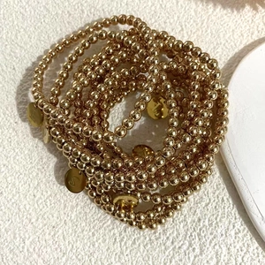 Gedetailleerde weergave van gouden kralenarmbanden met gegraveerde bedels op stenen ondergrond