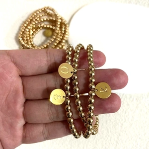 Close-up van gouden kralenarmbanden met dubbelzijdig gegraveerde alfabet hangers