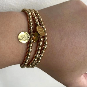 Detail van drielaagse gouden kralenarmbanden met gegraveerde hangers met letters B en D