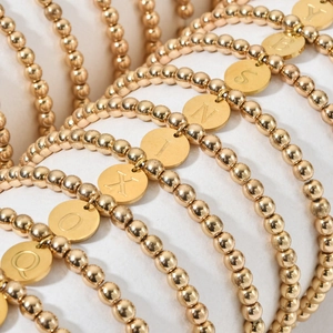 Minimalistische gouden kralenarmbanden met gegraveerde letterhangers in gelaagde layout