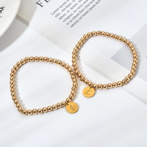 Detail van vergulde kralenarmbanden met gegraveerde bedeltjes van de letters E en L