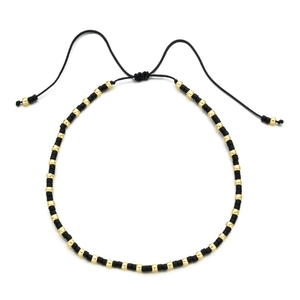 Detail of bohemian handmade beaded bracelet with black beads and gold accents on white base