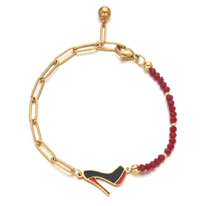Detail of a gold paperclip chain and red beads bracelet with a high heel pendant charm