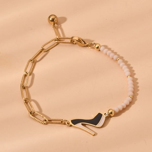 Detail of a gold paperclip chain bracelet with pink beads and a high heel shoe charm