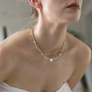 Close-up of layered bohemian necklaces featuring gold paperclip chain and initial M pendant