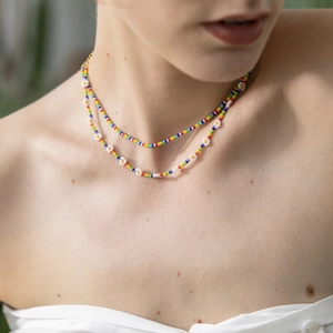 Detail of bohemian rainbow bead necklaces with white daisy charms on a model neck