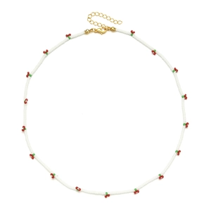 Detail of white beaded necklace with red cherry charms and golden lobster clasp