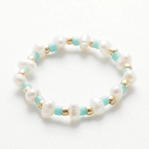 Dettaglio anello fatto a mano con perle d'acqua dolce e perline blu su sfondo bianco